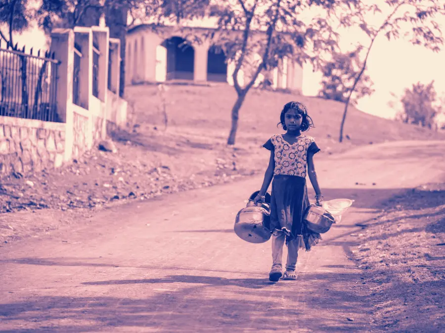 A girl walking home from the village well with a water pot